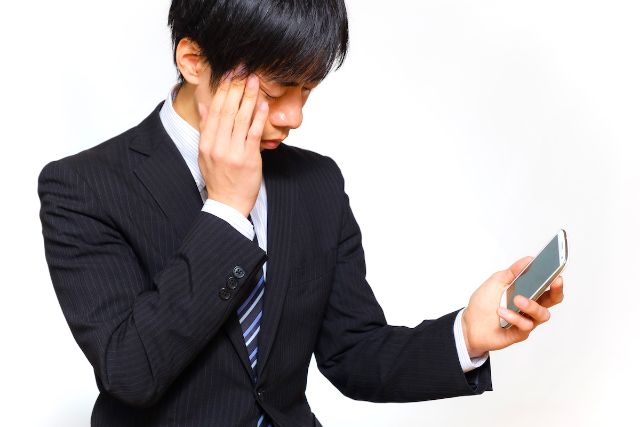 スマートフォンを見ながら蟀谷を押さえる男性